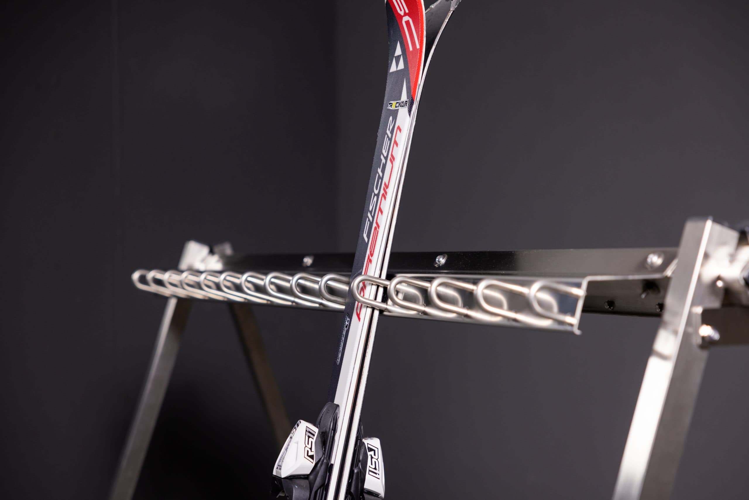 Vertical alpine skis with red and white graphics secured in a metal rack against a dark background.